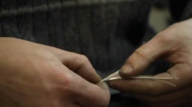 Yakın plan kuyumcu yeni bir ürüne başlıyor, gümüş bir bilezik dokuyor, seçici odaklanıyor.