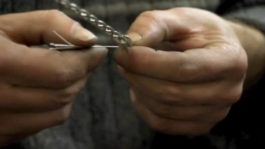 Yakın plan kuyumcu yeni bir ürüne başlıyor, gümüş bir bilezik dokuyor, seçici odaklanıyor.