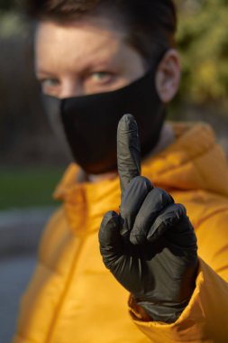 Korunaklı siyah maskeli orta yaşlı Avrupalı kadın Coronavirus COVID-19 salgını sırasında uyarı jesti yapıyor..