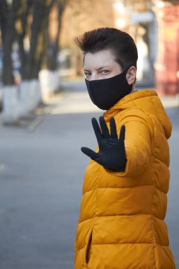 Korunaklı siyah maskeli orta yaşlı Avrupalı kadın Coronavirus COVID-19 salgını sırasında uyarı jesti yapıyor..