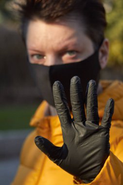 Korunaklı siyah maskeli orta yaşlı Avrupalı kadın Coronavirus COVID-19 salgını sırasında uyarı jesti yapıyor..