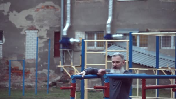大胡子男子 有强壮的肌肉手臂 在室外锻炼 做俯卧撑 老年男子在水平杠上做拉力运动 — 图库视频影像