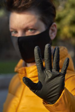 Korunaklı siyah maskeli orta yaşlı Avrupalı kadın Coronavirus COVID-19 salgını sırasında uyarı jesti yapıyor..