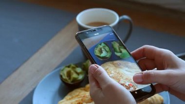 Kadın blogcu, akıllı telefon, ketojenik beslenme, gerçek hayat ve seçici odaklanma ile omlet ve avokado kahvaltısı yapar.