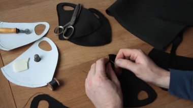 Beyaz, olgun sakallı adam evde ev yapımı koruyucu yüz maskesi dikiyor. Koronavirüs salgınına karşı koruma sağlıyor.