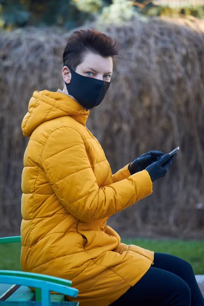 Korunaklı siyah maskeli ve eldivenli orta yaşlı Avrupalı kadın Coronavirus COVID-19 salgını sırasında dışarıda akıllı telefon tutuyor. — Stok fotoğraf