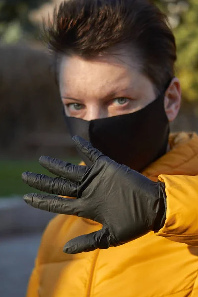Mujer europea de mediana edad con máscara negra protectora hace un gesto de advertencia durante la epidemia de coronavirus COVID-19. Mujer enferma que usa protección durante pandemia . —  Fotos de Stock