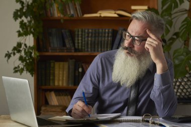 Mesafe öğrenme kavramı. Öğretmen dizüstü bilgisayarına bakıyor ve not defterine notlar yazıyor, seçici odaklanma