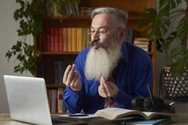 Mesafe öğrenme kavramı. Çılgına dönmüş öğretmen dizüstü bilgisayara bakıyor ve elleriyle el kol hareketi yapıyor, seçici odaklanma.