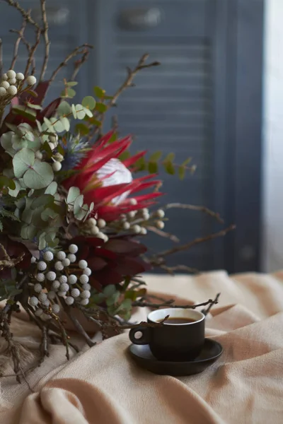 Cup of coffee and exotic bouquet without packaging stands on table with beige tablecloth, holiday morning concept, selective focus