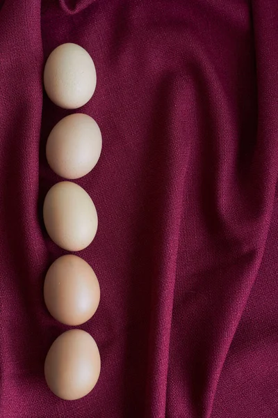 Natural eggs on red tablecloth, few brown chicken eggs lie on burgundy tablecloth, selective focus