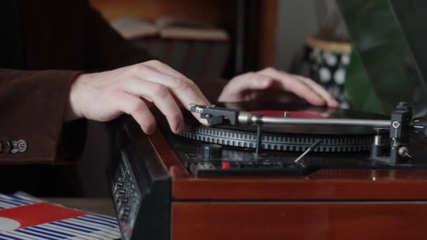 Gros plan de mains masculines mettant un disque dans la platine, platine rétro jouant dans la bibliothèque à domicile, mise au point sélective — Video