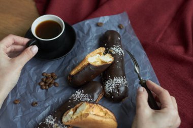 Vanilya kremalı eklerleri yiyen kadın, çikolatalı geleneksel Fransız eklerleri ve bir fincan espresso, seçici odaklanma..