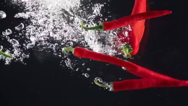 Warme pepers die in het water vallen. Langzame beweging — Stockvideo