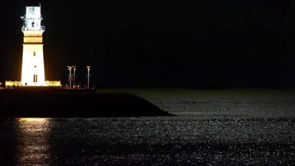 Faro en la noche, la luz de la luna refleja en el mar . — Vídeo de stock