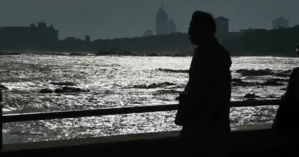 Qingdao China-juli 12, 2017:4 k mensen wandeling langs de kust op de schemering, kust stedelijke gebouw & golvende Oceaan — Stockvideo