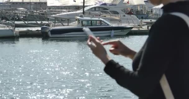 4k Una ragazza che utilizza uno smartphone al mare, yacht e vela nel porto . — Video Stock