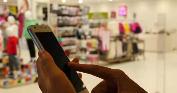 4 k A vrouw met behulp van een smartphone tegen Clothing store, winkelcentrum & supermarkt. — Stockvideo