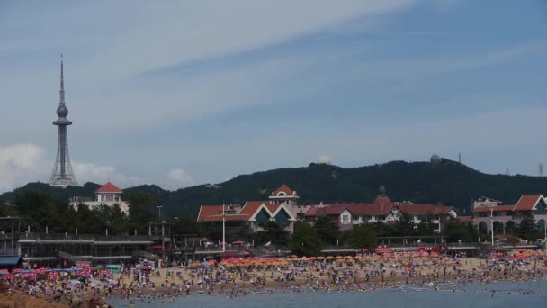 China-Aug 08, 2017:A veel mensen op druk badstrand. China's Qingdao City.high toren op voor — Stockvideo