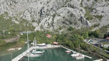 Güneşli bir yaz gününde Karadağ 'ın Boka-Kotor körfezindeki küçük bir yat limanının havadan çekilmiş görüntüleri. Denizin suları zümrüt, arka planda dağlar görünür.