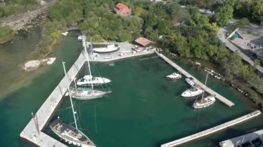 Güneşli bir yaz gününde Karadağ 'ın Boka-Kotor körfezindeki küçük bir yat limanının havadan çekilmiş görüntüleri. Denizin suları zümrüt, arka planda dağlar görünür.