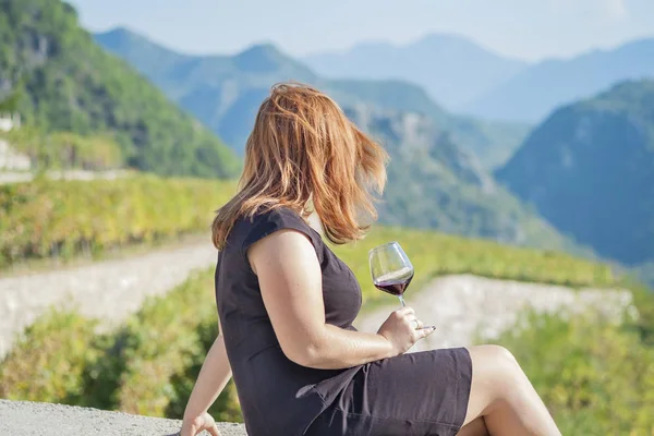 Kızıl saçlı, genç, tombul kadın elinde bir bardak kırmızı şarapla oturuyor. Telifsiz Stok Fotoğraflar