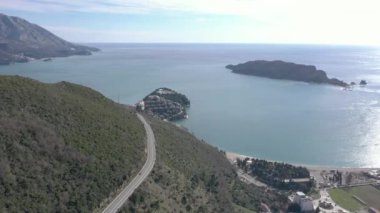 Arabaların sürdüğü dar ve dolambaçlı bir dağ yolunun hava görüntüsü. Sağ tarafta küçük adaları olan mavi denizi görebilirsiniz.