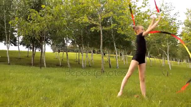 La chica se dedica a la gimnasia rítmica con cinta en la naturaleza — Vídeos de Stock