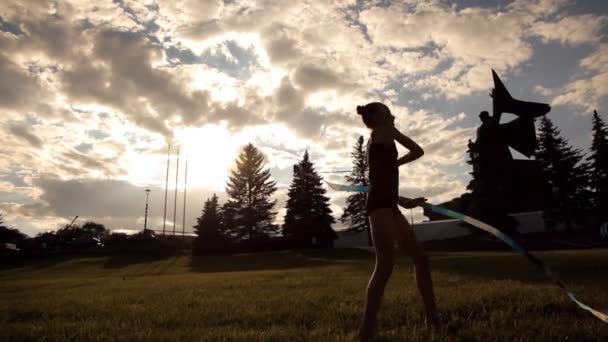 La chica se dedica a la gimnasia artística con una cinta en el parque de la cultura — Vídeos de Stock