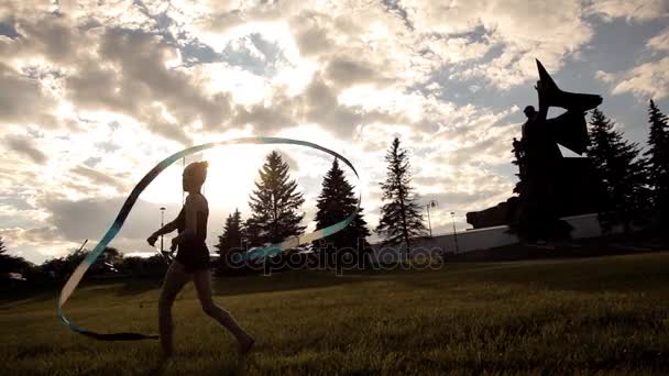 Flickan är engagerad i artistisk gymnastik med ett band i parken av kultur — Stockvideo