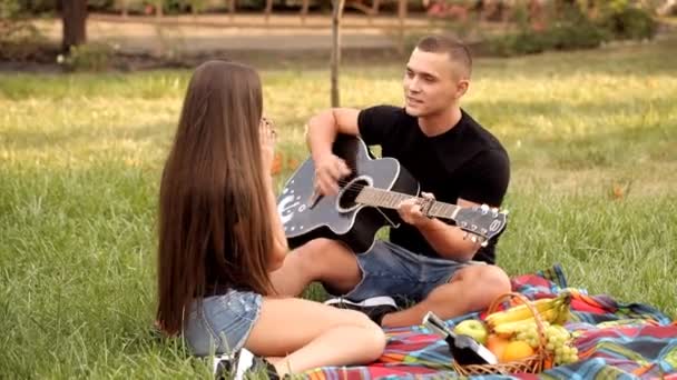 Genç adam onun kız arkadaşı gitar bir piknikte çalış. — Stok video