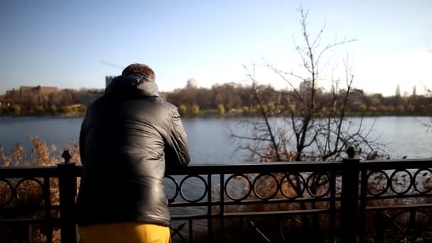 岸壁の上に立って湖を見て物思いにふける若い男 — ストック動画