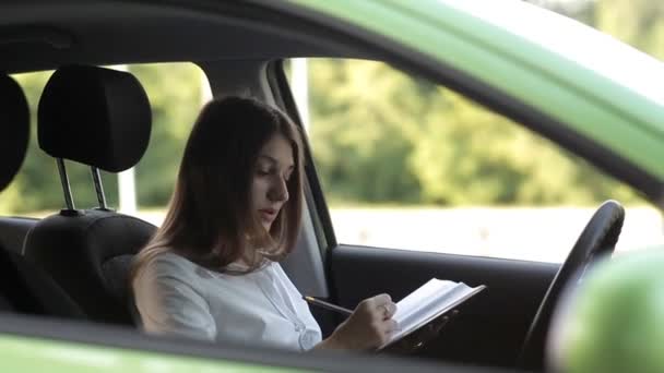 Business tjej, spelar medan i bilen, i en anteckningsbok för arbete — Stockvideo