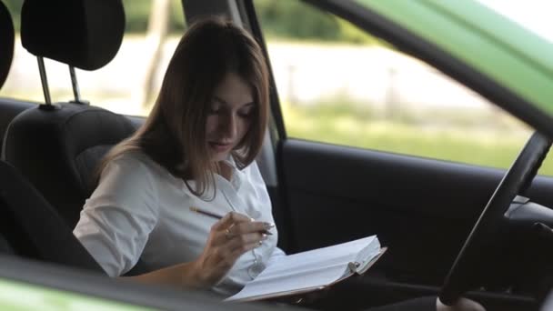 Biznes dziewczynka, w samochodzie, zapisuje w zeszycie do pracy — Wideo stockowe