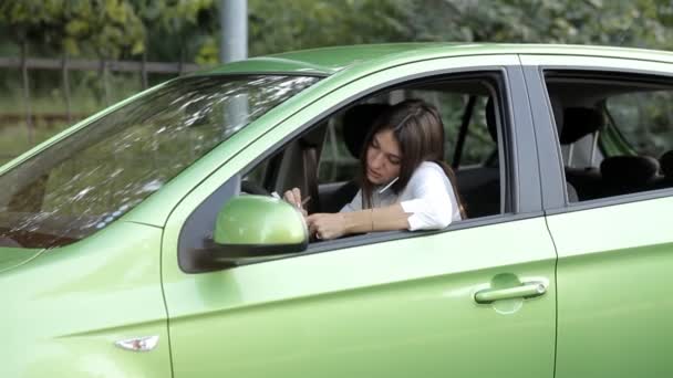 Meisje in een auto praten aan de telefoon over een bedrijf en het maken van notities in een notitieblok — Stockvideo