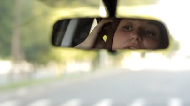 Het meisje achter het stuur van de auto kijkt in de spiegel — Stockvideo