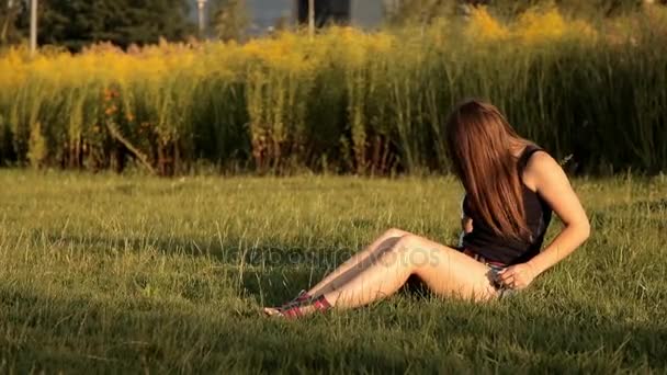 Jong meisje zit op een grasveld in het park en haar hond kusjes — Stockvideo