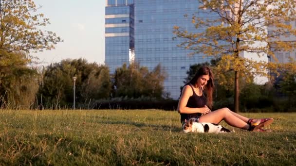 Krásná dívka, sedící se psem v parku při západu slunce