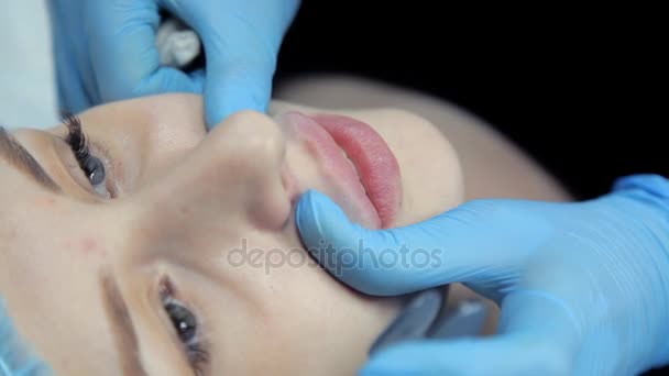 The beautician smoothes botox in the lips of a young girl after the injection. Lip augmentation procedure. — Stock Video