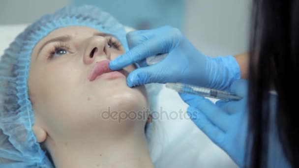 Косметическая девушка разглаживает ботокс в губах девушки после инъекции. Увеличение губ — стоковое видео