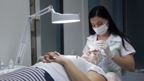 O cosmetician lubrifica o creme de cara de menina antes da biorevitalização. O procedimento para a restauração de processos na pele — Vídeo de Stock