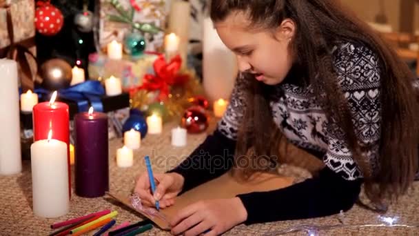 Una niña en un ambiente festivo escribe una carta a Santa Claus con sus deseos para el nuevo año — Vídeos de Stock