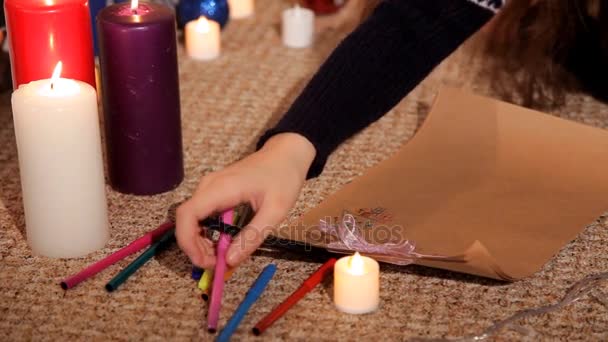Menina em um ambiente festivo em uma folha de papel desenha um cartão de Natal Papai Noel — Vídeo de Stock