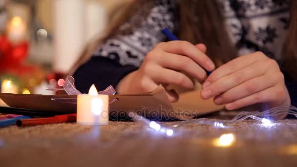 Bambina in un ambiente festivo su un foglio di carta disegna un biglietto di Natale Babbo Natale — Video Stock