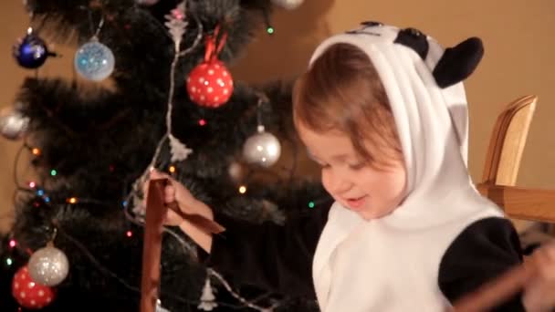 Niño abre un regalo de Año Nuevo cerca de un árbol de Navidad — Vídeos de Stock