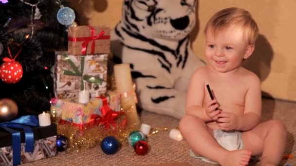 Een klein kind speelt in de buurt van een kerstboom — Stockvideo