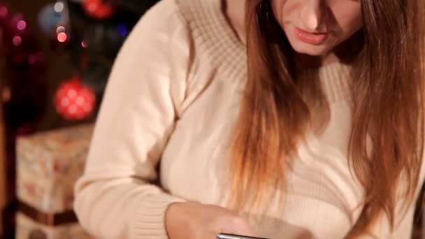 В праздничной новогодней обстановке девушка пользуется мобильным телефоном — стоковое видео