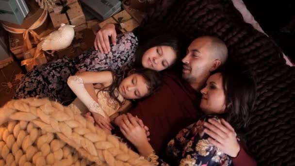 El padre con su esposa y dos personas está acostado en la cama en el ambiente del Año Nuevo. Familia feliz en Nochebuena — Vídeos de Stock