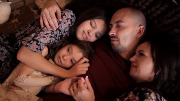 De vader met zijn vrouw en twee mensen is liggend op het bed in de sfeer van het nieuwe jaar. Op kerstavond en gelukkige familie — Stockvideo