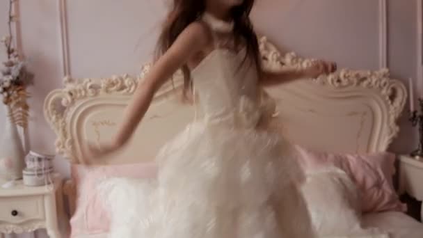 Kleines Mädchen im schneeweißen Kleid springt auf ein luxuriöses Bett — Stockvideo